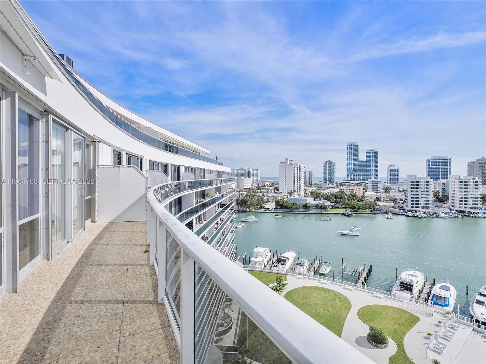 A curved balcony overlooks a marina with boats, a grassy area, and city buildings — 900 Bay Dr # 1012, Miami Beach FL 33141, MIAMI BEACH, FL