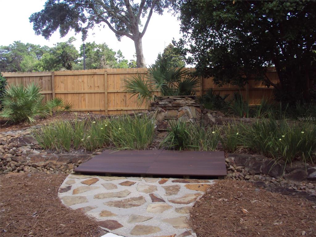 A backyard features a stone path leading to a wooden platform near a stone fountain — 101 SAND OAK BOULEVARD, PANAMA CITY BEACH, FL