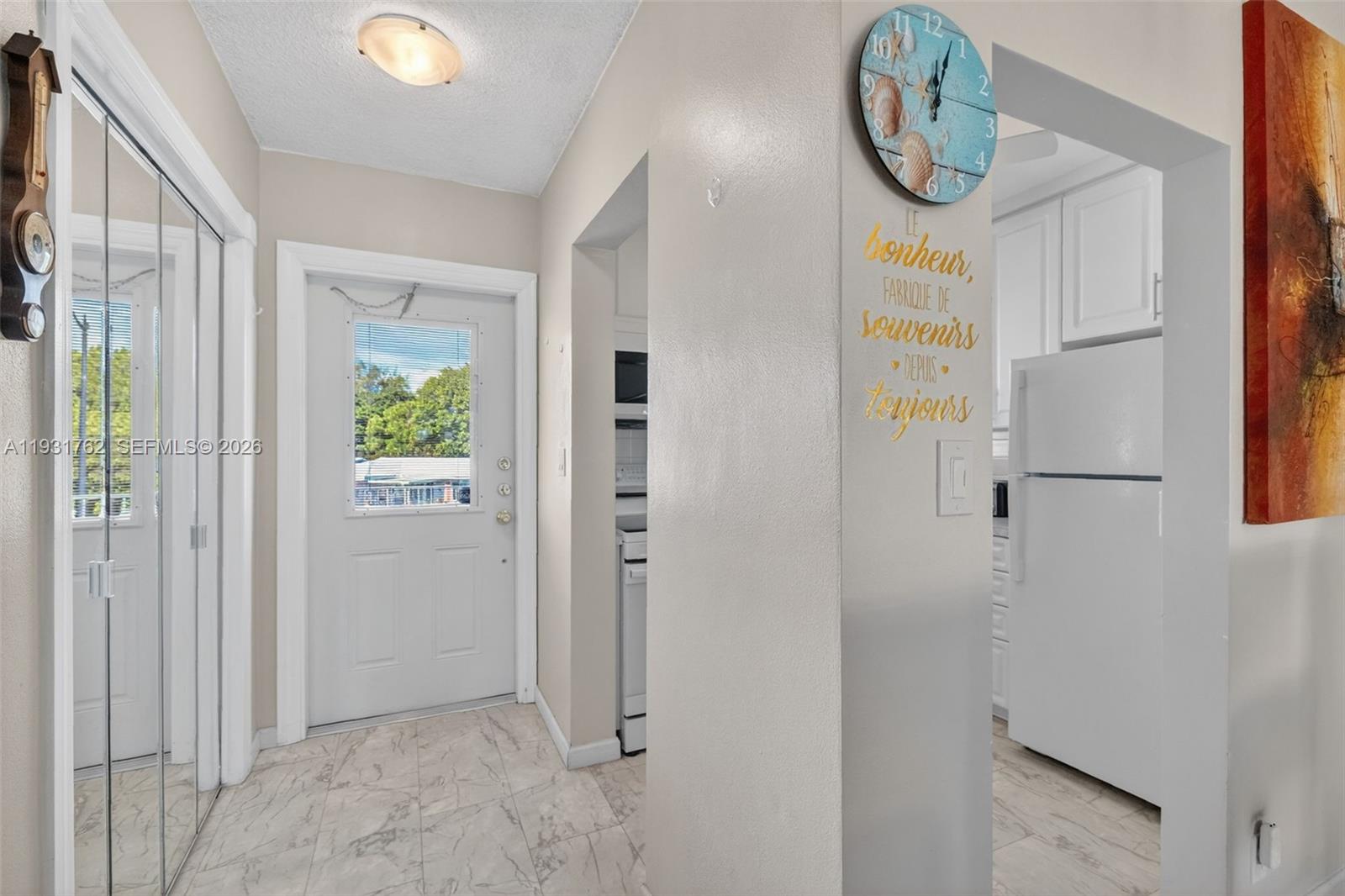 An entryway with marble-look tile flooring leads to a kitchen with white appliances and cabinetry — 2650 W Golf Blvd # 259, Pompano Beach FL 33064, POMPANO BEACH, FL