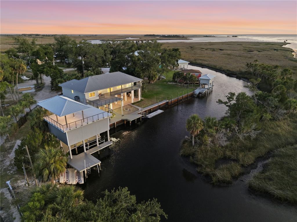 An aerial view shows a waterfront house with a boat dock and deck at sunset — 38 SE 195TH STREET, SUWANNEE, FL