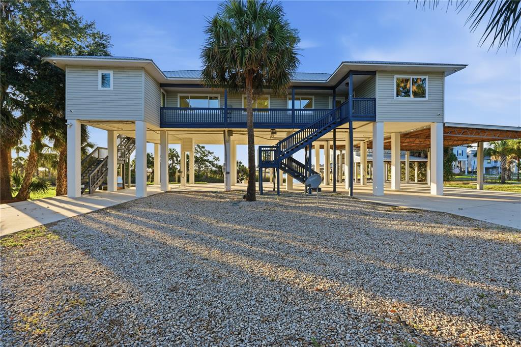 A stilt house with light siding, a blue staircase, and a gravel driveway underneath — 38 SE 195TH STREET, SUWANNEE, FL