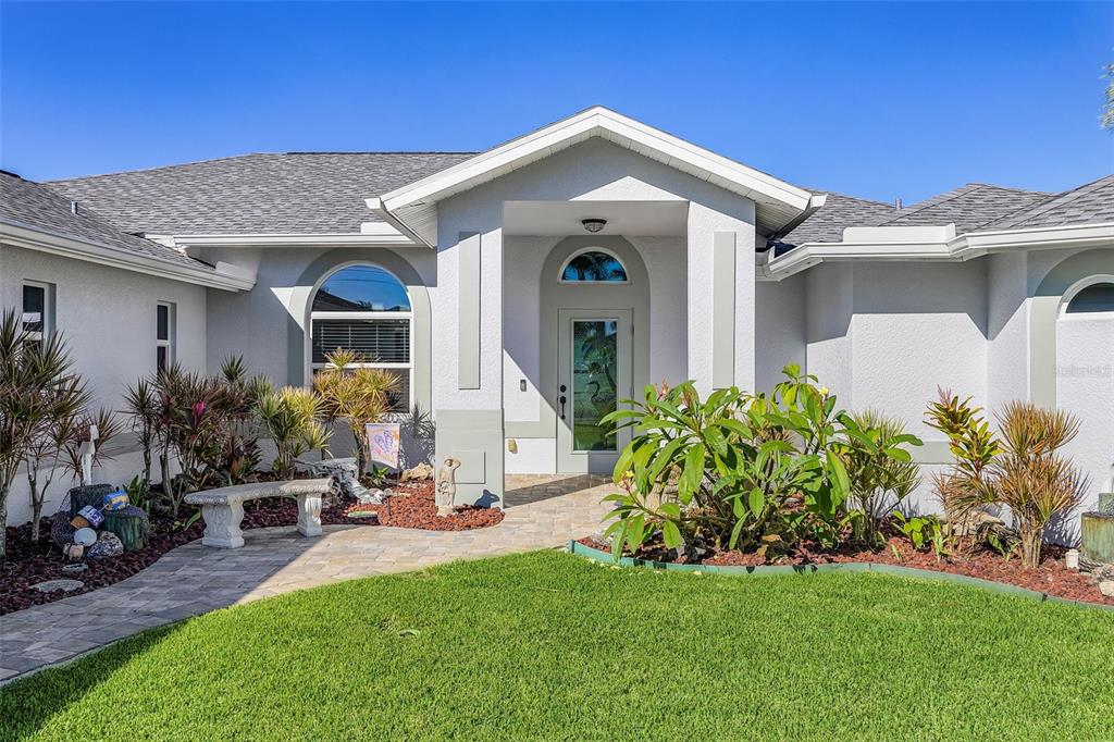The exterior of a single-story house features a covered entryway, a stone walkway, and landscaping — 430 NW 39TH AVENUE, CAPE CORAL, FL
