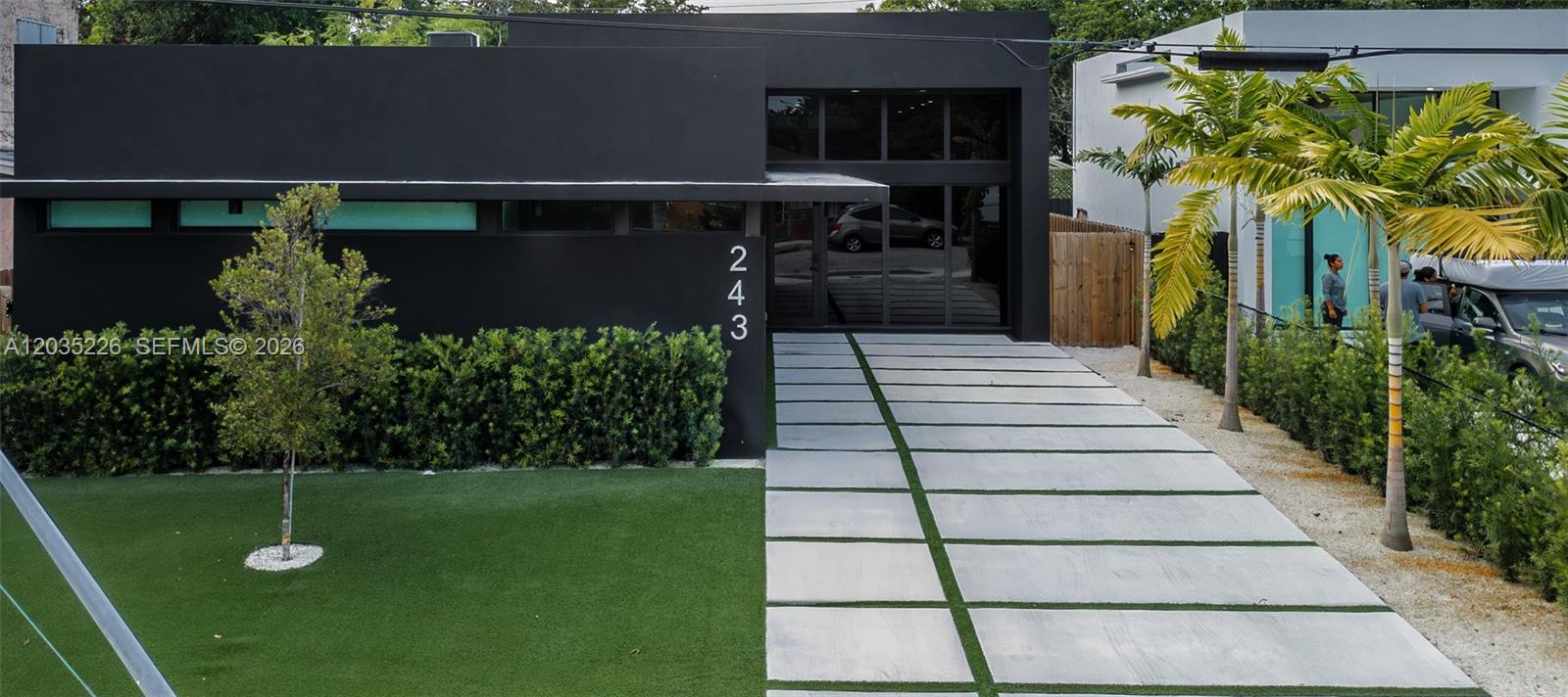 A modern black house features a paved driveway, artificial turf, and palm trees — 243 NW 42nd St, Miami FL 33127, MIAMI, FL