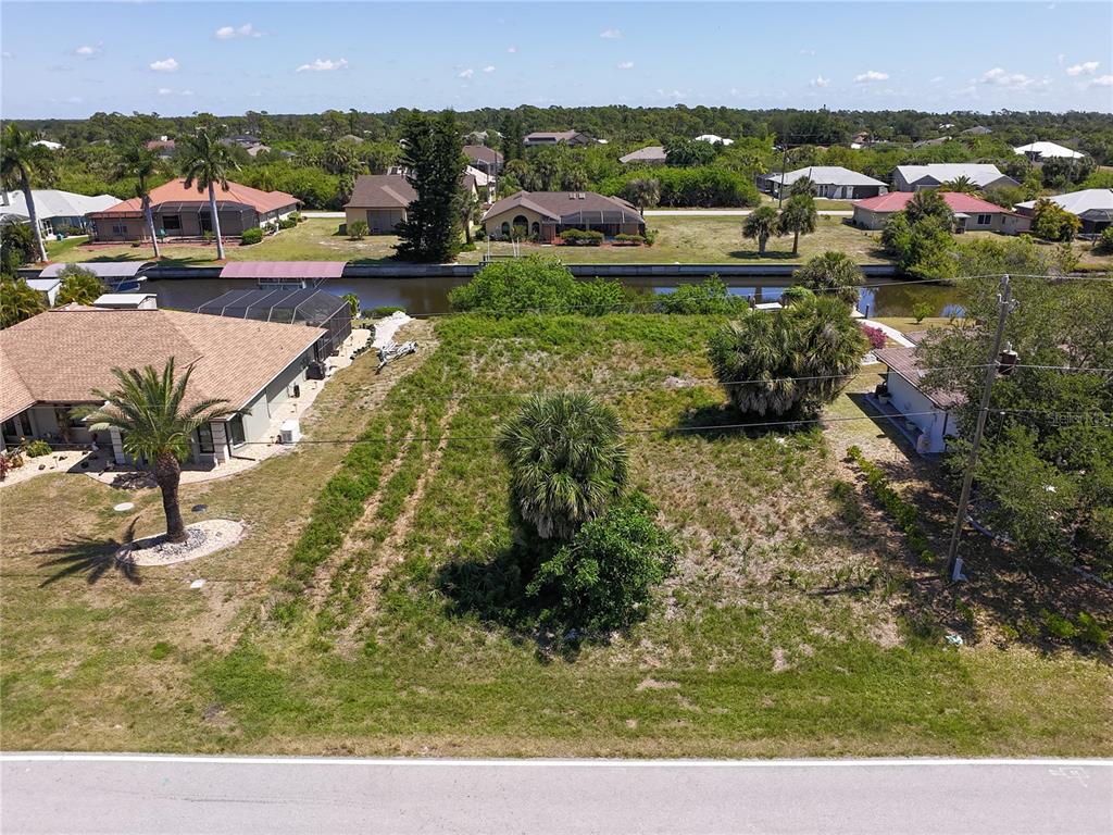 An aerial view shows a vacant, grassy residential lot situated between two houses near a canal — 17360 OHARA DRIVE, PORT CHARLOTTE, FL