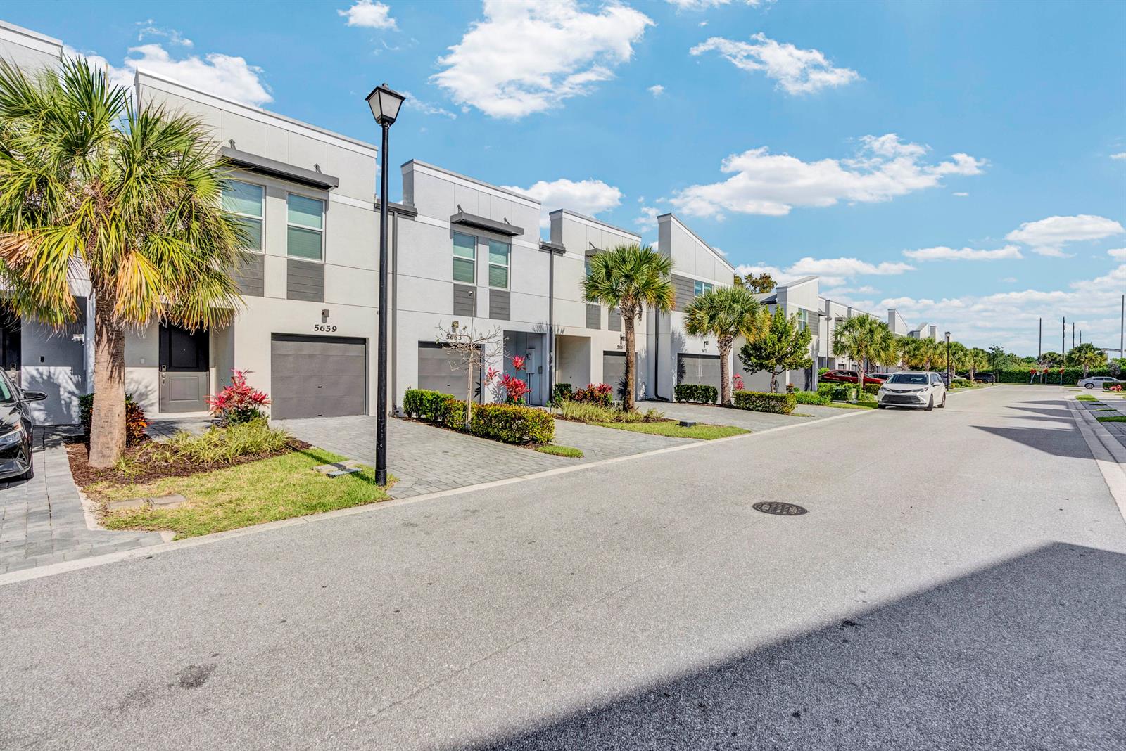 A row of modern townhouses with gray garages, paved driveways, and palm trees under a sky — 5659 Enclave Drive, Riviera Beach FL 33407, RIVIERA BEACH, FL