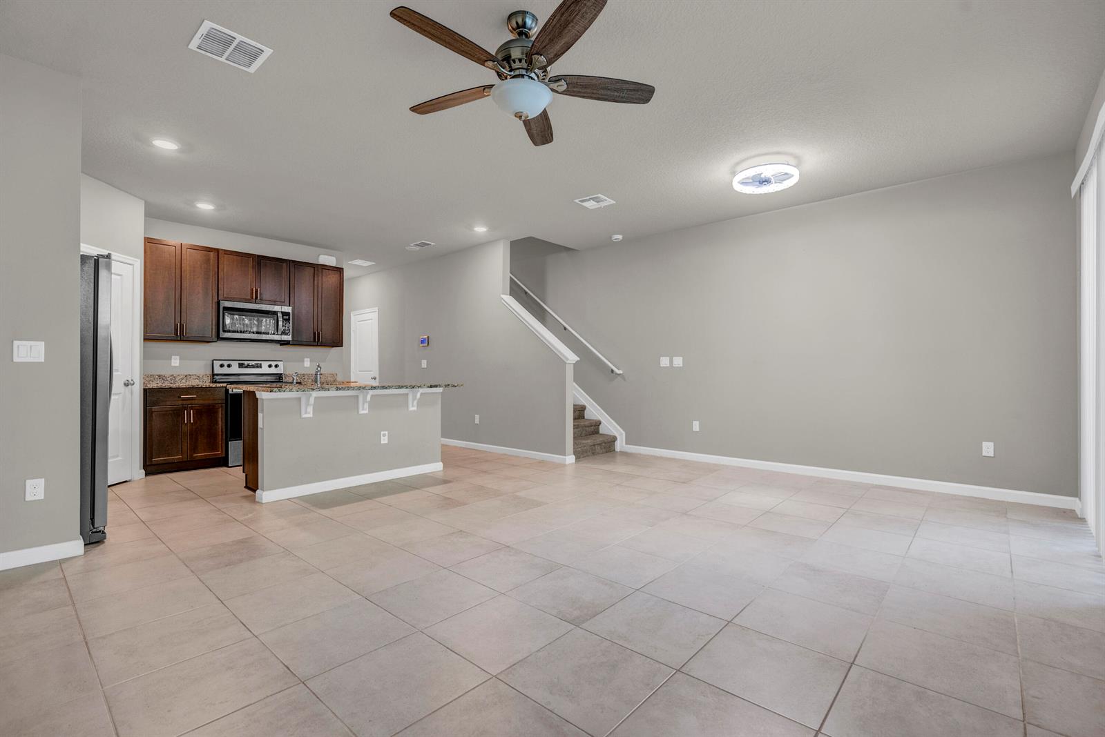 An open-concept kitchen and living area featuring tile flooring, dark wood cabinets, and a staircase — 5659 Enclave Drive, Riviera Beach FL 33407, RIVIERA BEACH, FL