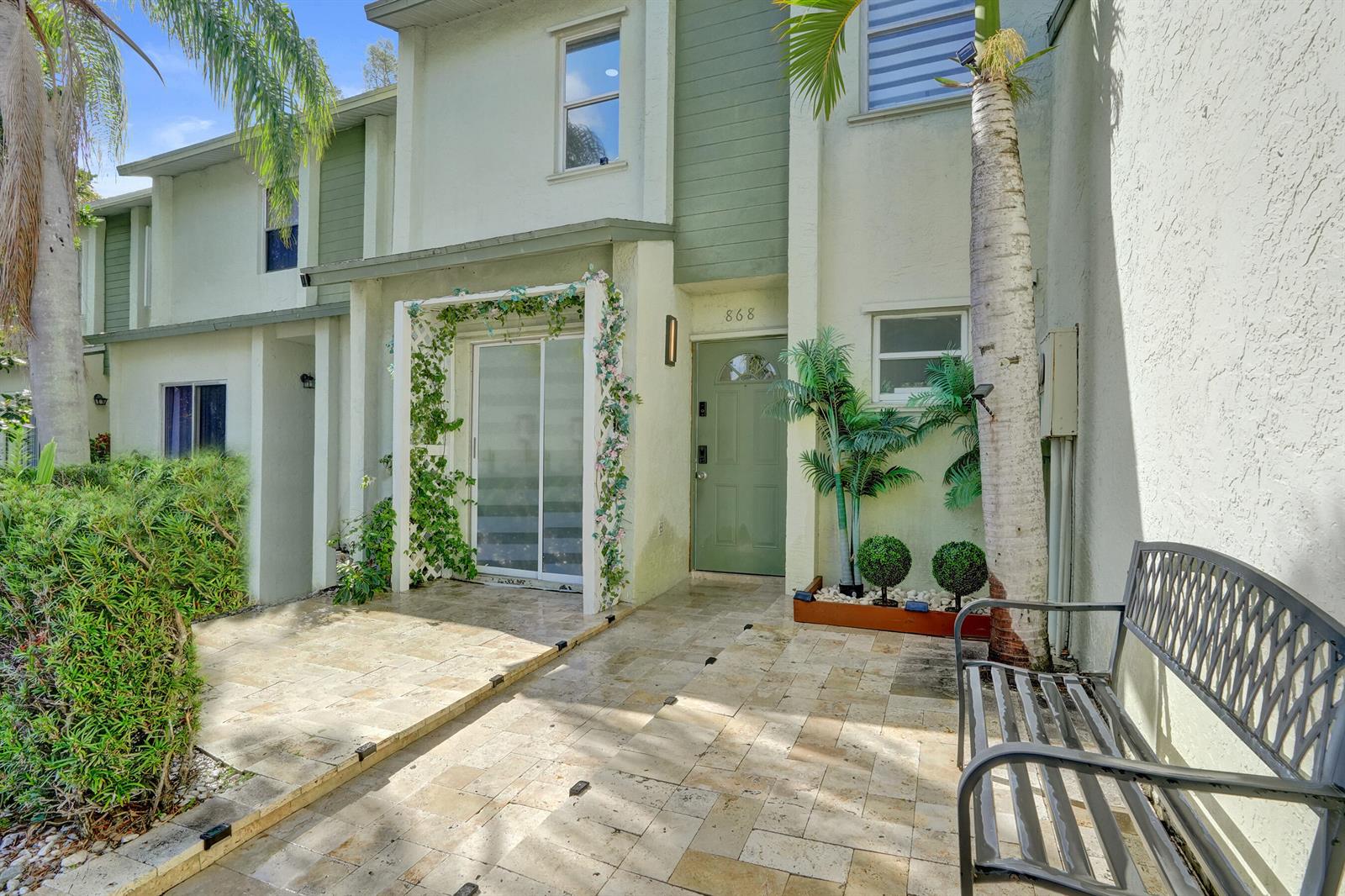 The exterior of a two-story townhouse features a tiled patio, a green front door, and landscaping — 868 Crystal Lake Drive, Deerfield Beach FL 33064, DEERFIELD BEACH, FL