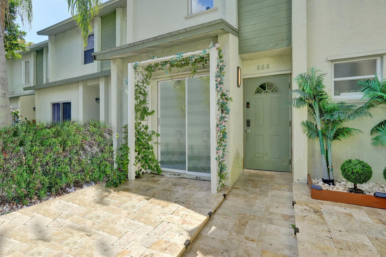The exterior of a townhouse features a green front door, a stone patio, and a trellis — 868 Crystal Lake Drive, Deerfield Beach FL 33064, DEERFIELD BEACH, FL