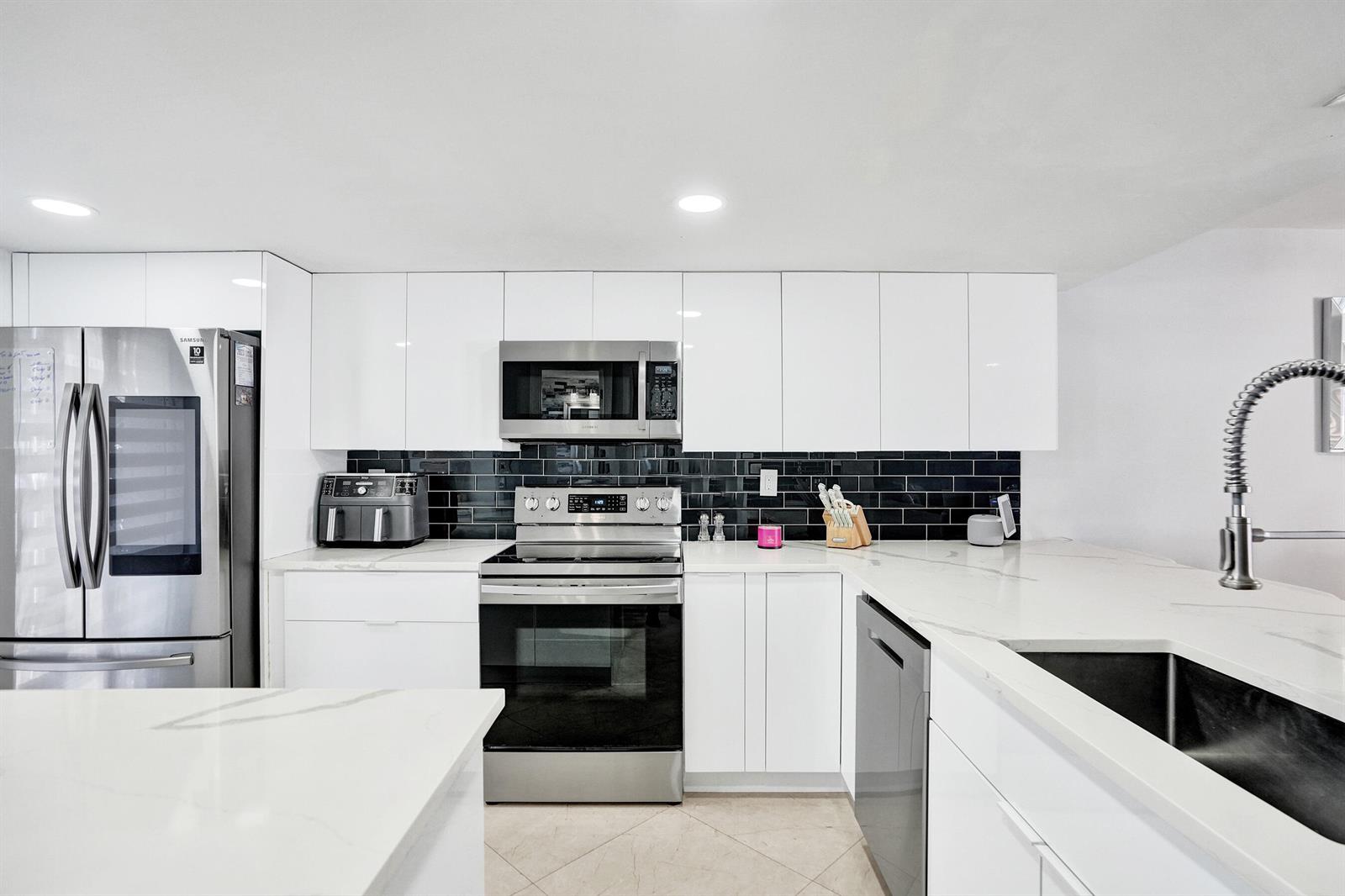 A modern kitchen features white cabinets, stainless steel appliances, and a black subway tile backsplash — 868 Crystal Lake Drive, Deerfield Beach FL 33064, DEERFIELD BEACH, FL