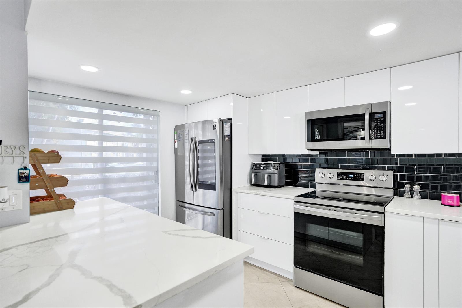 A modern kitchen features white cabinets, stainless steel appliances, and a white marble-patterned island — 868 Crystal Lake Drive, Deerfield Beach FL 33064, DEERFIELD BEACH, FL