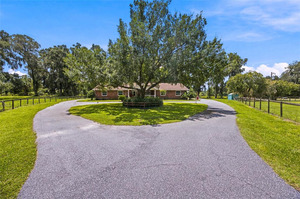 A brick house sits behind a circular driveway with a large tree in the center — 690 SW 165TH STREET, OCALA, FL