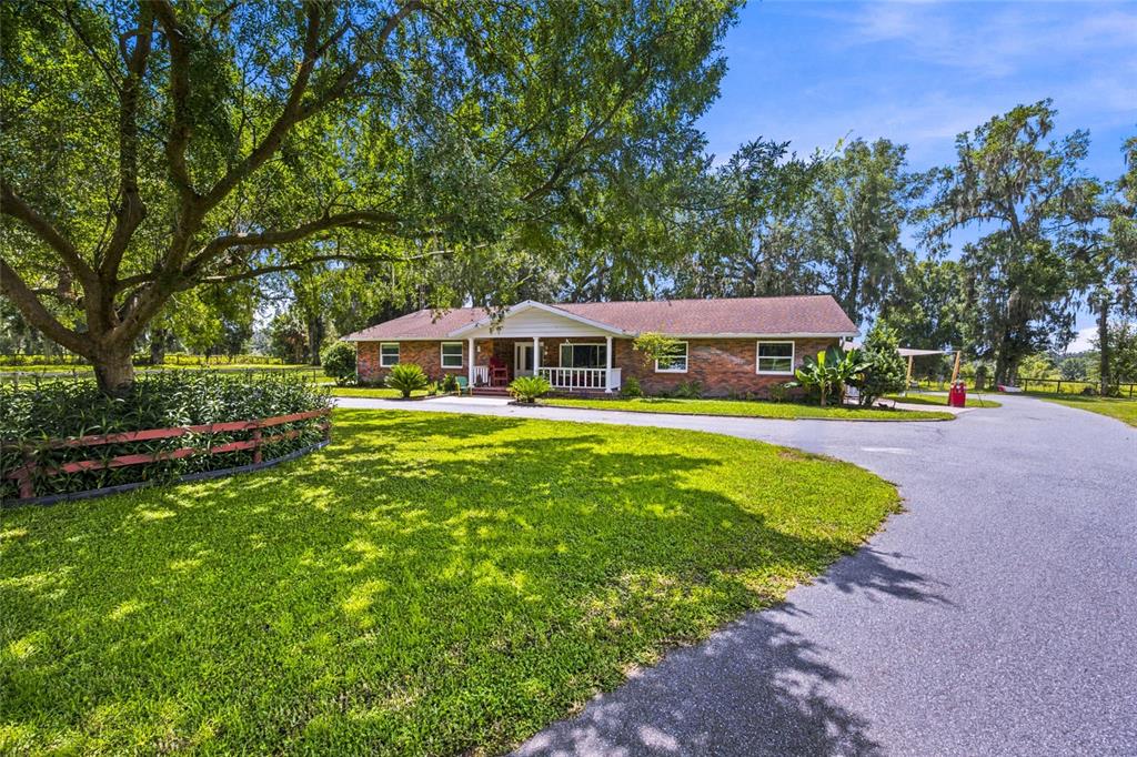A single-story brick house with a white porch sits behind a large tree and lawn — 690 SW 165TH STREET, OCALA, FL