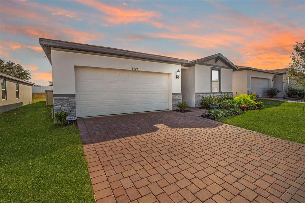 A single-story house with a white stucco exterior, stone accents, and a brick paver driveway — 2409 WHITE TAIL STREET, DAVENPORT, FL
