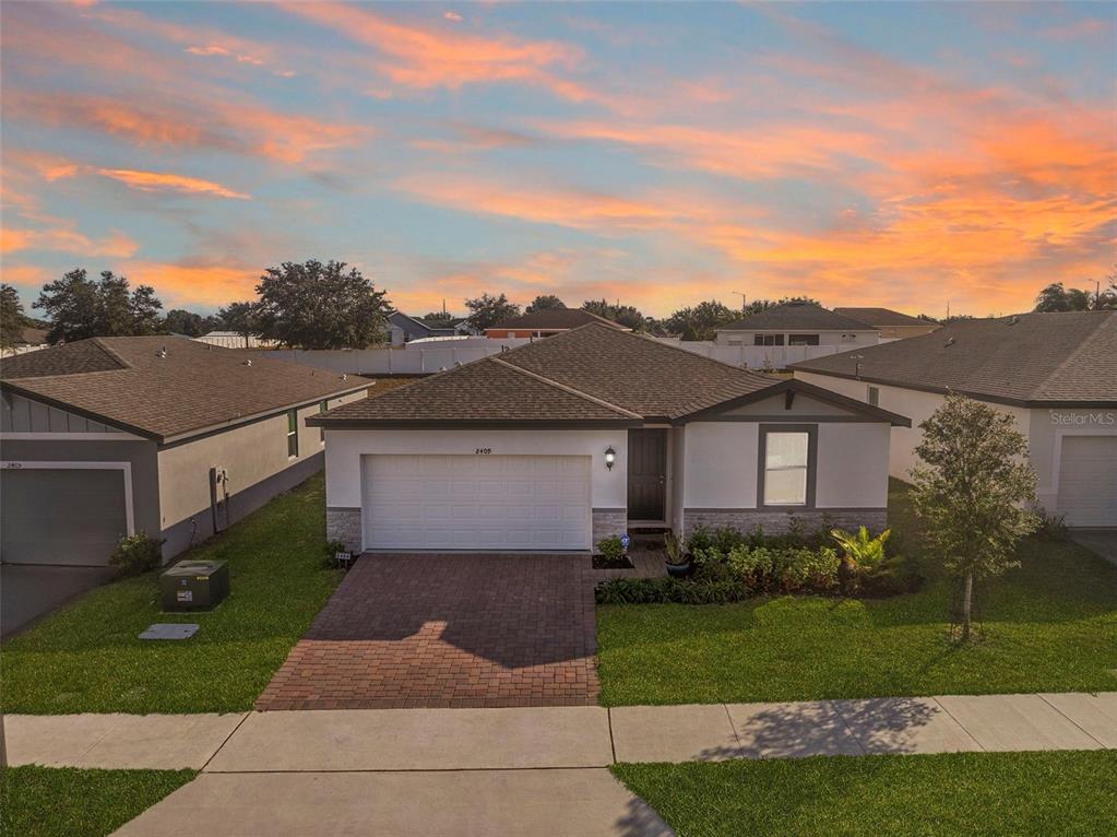 A single-story suburban house with a brick driveway and a two-car garage at sunset — 2409 WHITE TAIL STREET, DAVENPORT, FL