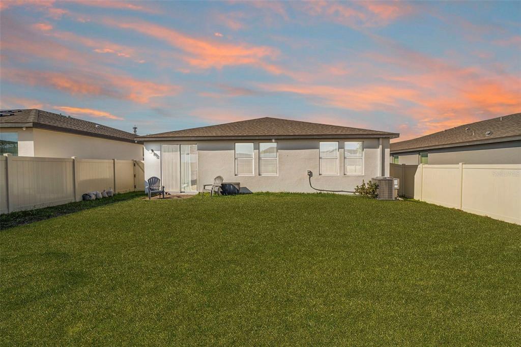 The exterior rear view of a single-story house with a fenced yard and lawn — 2409 WHITE TAIL STREET, DAVENPORT, FL