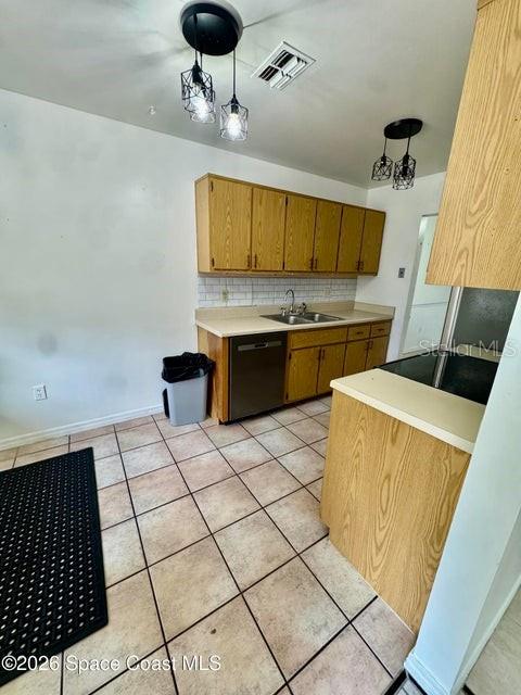 A kitchen features light wood cabinets, tile flooring, and a stainless steel dishwasher — 1220 CHENEY HIGHWAY UNIT D, TITUSVILLE, FL