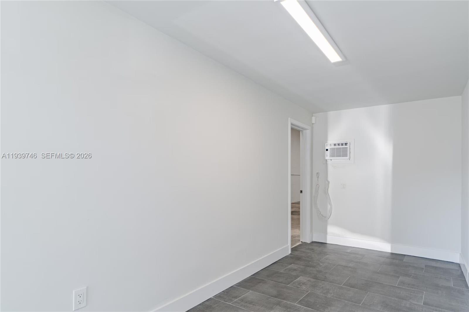 A room with white walls, gray tile flooring, a wall-mounted air conditioner, and a doorway — 453 W 28th St, Hialeah FL 33010, HIALEAH, FL