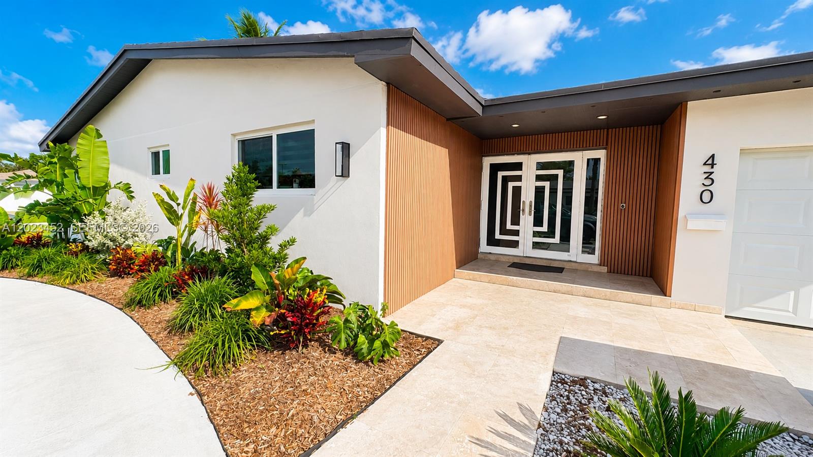 The exterior of a modern house features a white facade, wood-slat accents, and double doors — 430 NE 145th St, Miami FL 33161, MIAMI, FL