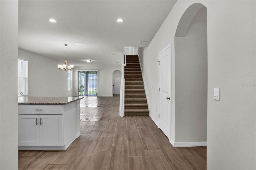 A kitchen island with granite countertops sits in front of a staircase and open living area — 16845 HOBE SOUND COURT, WINTER GARDEN, FL