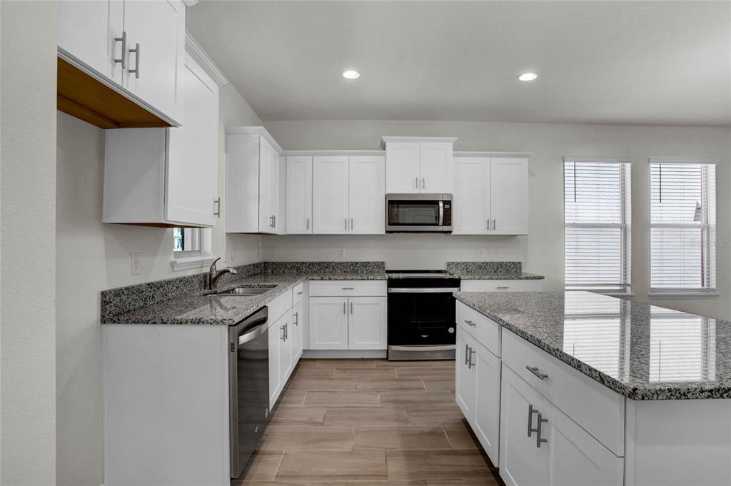 A kitchen features white cabinets, granite countertops, stainless steel appliances, and light wood-look flooring — 16845 HOBE SOUND COURT, WINTER GARDEN, FL