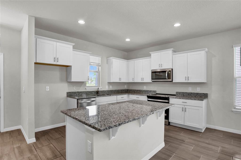 A kitchen features white cabinets, granite countertops, a center island, and wood-look tile flooring — 16845 HOBE SOUND COURT, WINTER GARDEN, FL