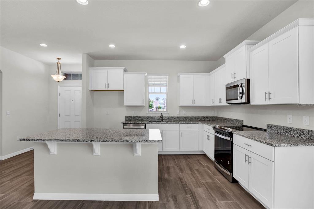 A kitchen with white cabinets, granite countertops, a center island, and wood-look flooring — 16845 HOBE SOUND COURT, WINTER GARDEN, FL