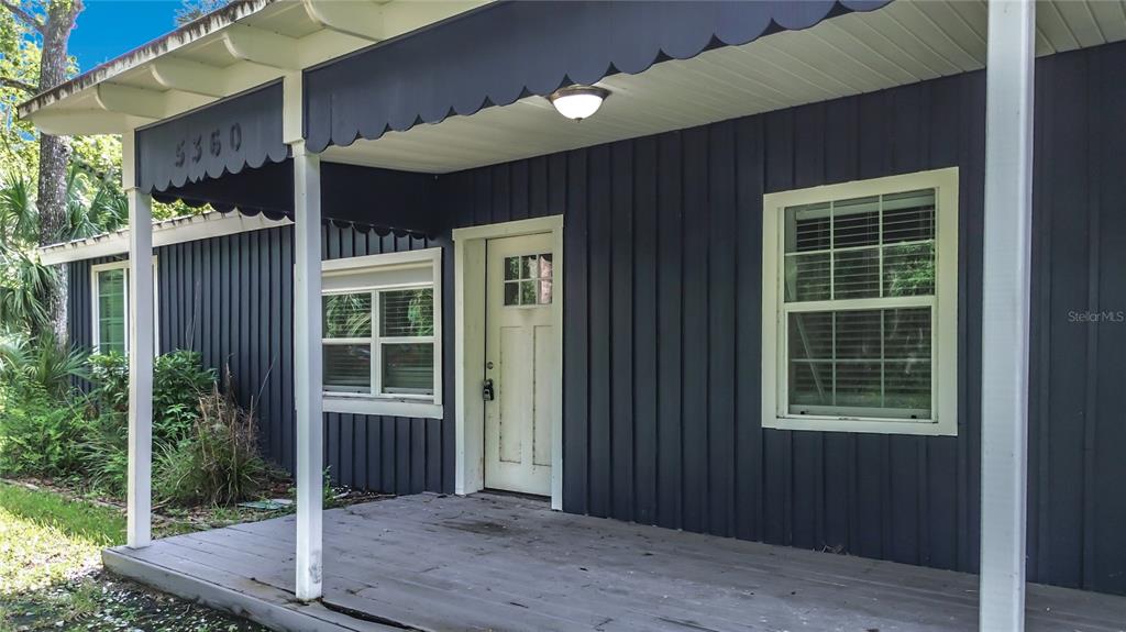 A dark blue house exterior features a covered porch with a scalloped awning and windows — 5360 S ELM AVENUE, HOMOSASSA, FL
