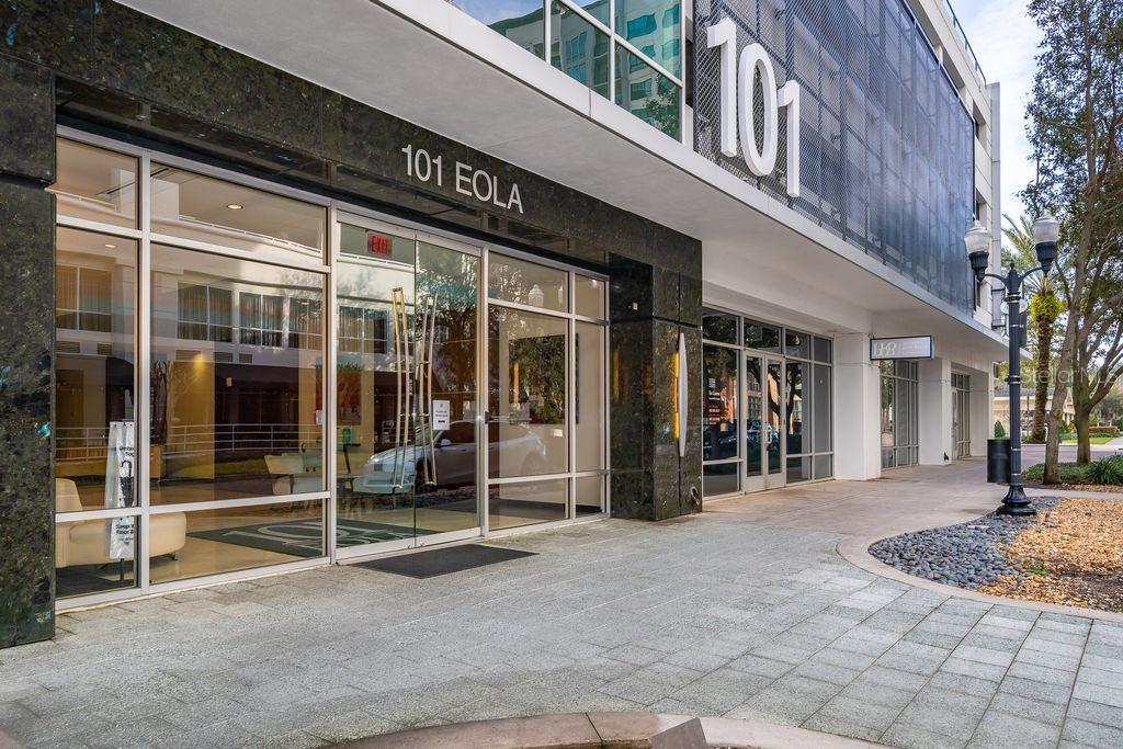 The exterior entrance of a modern commercial building features glass doors and stone tile flooring — 101 S EOLA DRIVE UNIT 707, ORLANDO, FL