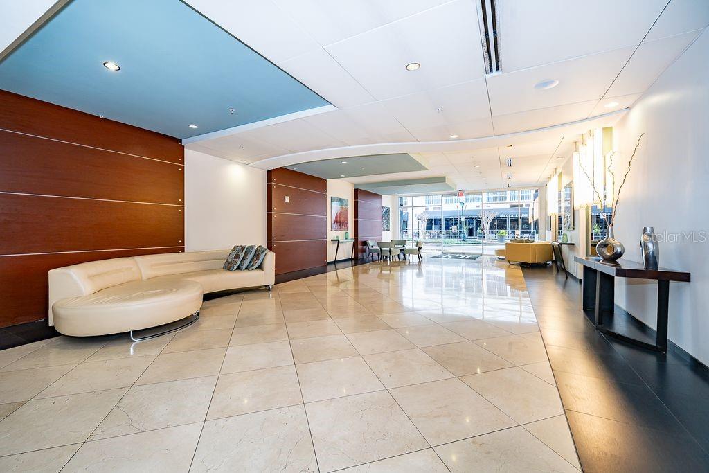 A modern building lobby features a curved cream sofa, tiled floors, and wood-paneled walls — 101 S EOLA DRIVE UNIT 707, ORLANDO, FL