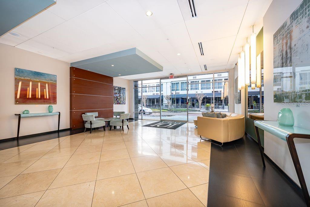A modern building lobby features tiled floors, a seating area, and large glass entrance doors — 101 S EOLA DRIVE UNIT 707, ORLANDO, FL