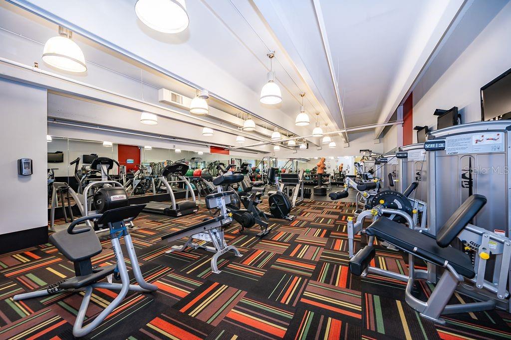 A gym features various exercise machines, a patterned carpet, and multiple hanging pendant lights — 101 S EOLA DRIVE UNIT 707, ORLANDO, FL