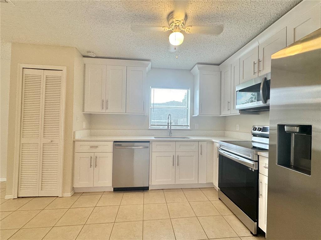 A kitchen features white cabinets, stainless steel appliances, tile flooring, and a ceiling fan — 1622 CIMARRON HILLS DRIVE, APOPKA, FL