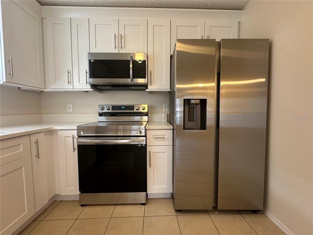 A kitchen features white cabinets, stainless steel appliances, and light-colored countertops — 1622 CIMARRON HILLS DRIVE, APOPKA, FL