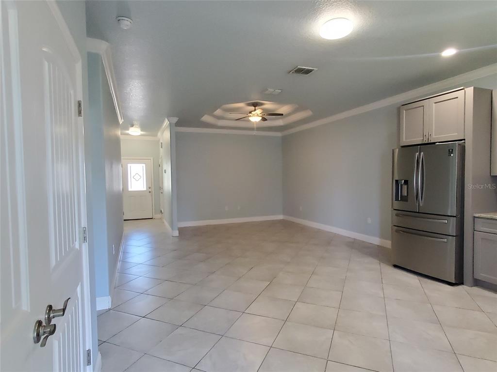 An open-concept room with light blue walls, tile flooring, a tray ceiling, and stainless refrigerator — 7 EMPIRE LANE UNIT B, PALM COAST, FL
