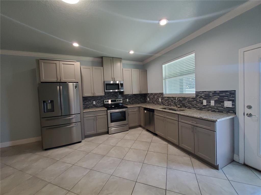 A kitchen features gray cabinets, stainless steel appliances, granite countertops, and a tiled backsplash — 7 EMPIRE LANE UNIT B, PALM COAST, FL