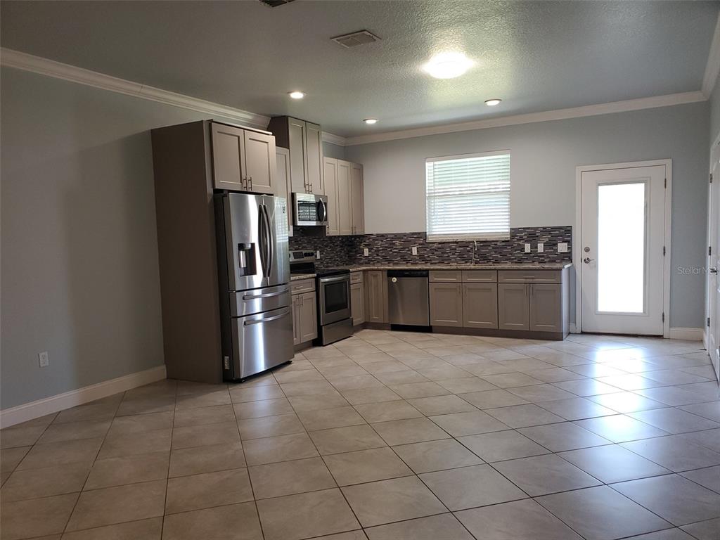 A kitchen features gray cabinets, stainless steel appliances, a tiled backsplash, and light-colored floor tiles — 7 EMPIRE LANE UNIT B, PALM COAST, FL