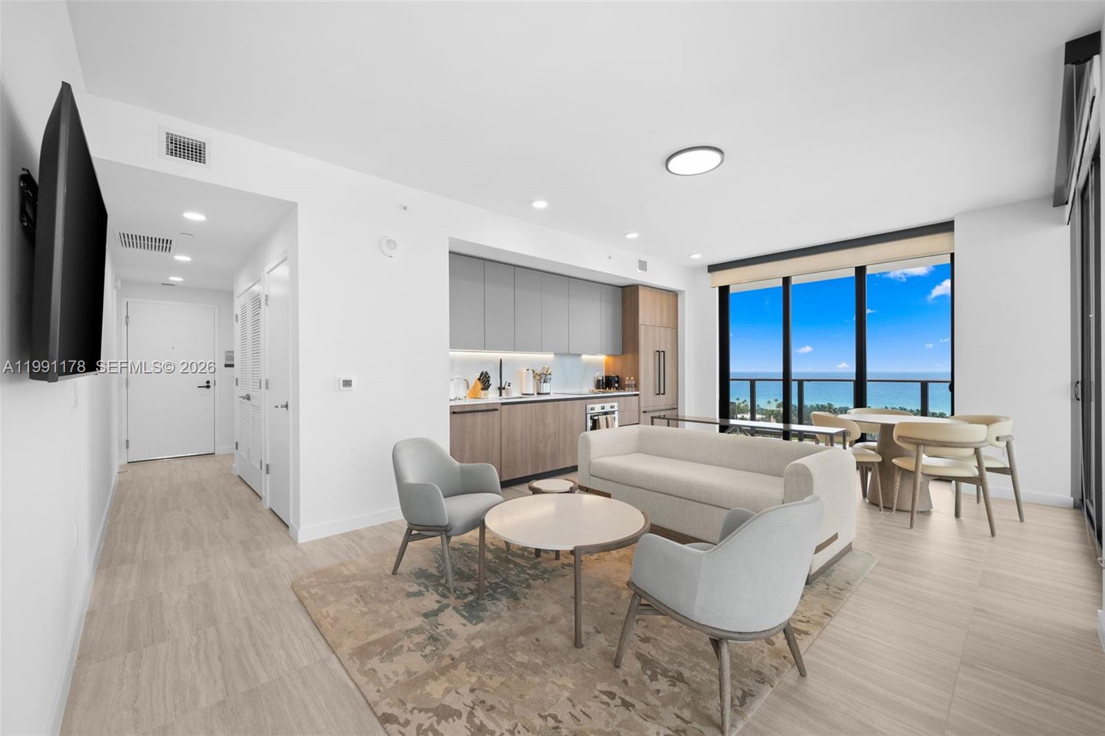 A modern living room and kitchen area features light wood flooring and ocean views — 580 72nd St # 1402, Miami Beach FL 33141, MIAMI BEACH, FL