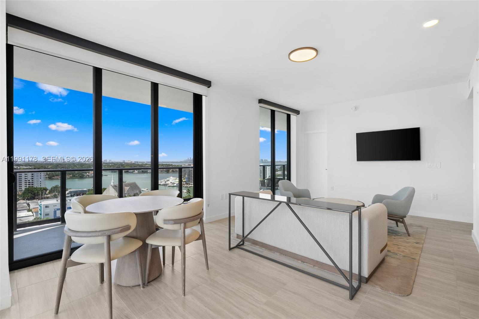 A modern living and dining area features floor-to-ceiling windows with a waterfront view — 580 72nd St # 1402, Miami Beach FL 33141, MIAMI BEACH, FL
