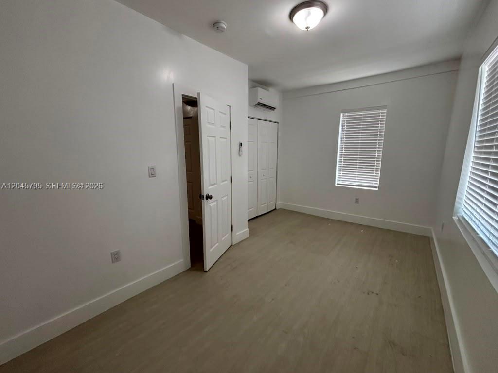 A bedroom features light-colored wood-look flooring, white walls, a closet, and a window with blinds — 1051 NW 2nd St # 15, Miami FL 33128, MIAMI, FL