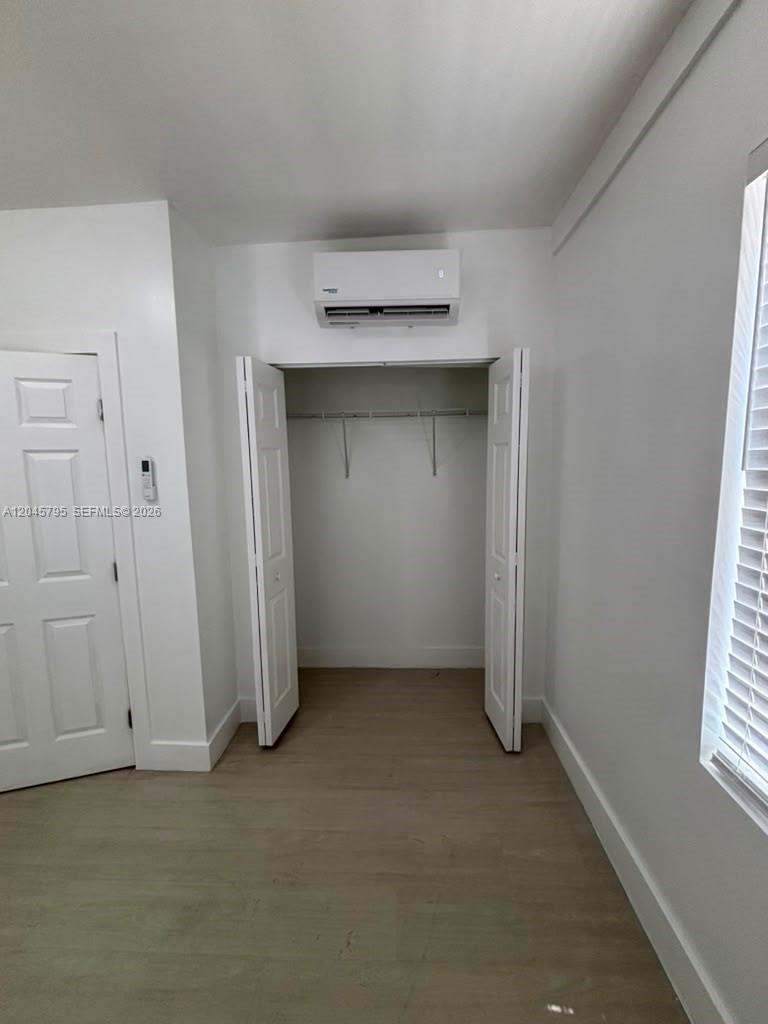 A bedroom features light wood-look flooring, a white closet, and a wall-mounted air conditioning unit — 1051 NW 2nd St # 15, Miami FL 33128, MIAMI, FL