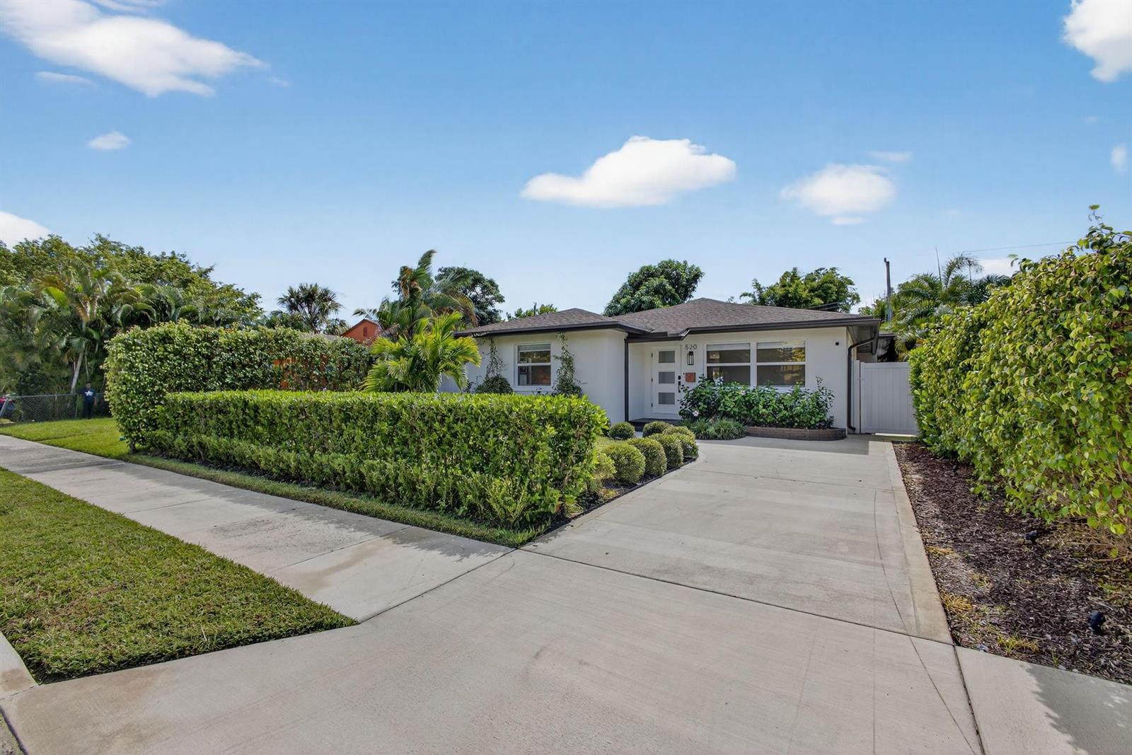 A single-story white house with a concrete driveway and manicured hedges under a blue sky — 520 36th Street, West Palm Beach FL 33407, WEST PALM BEACH, FL
