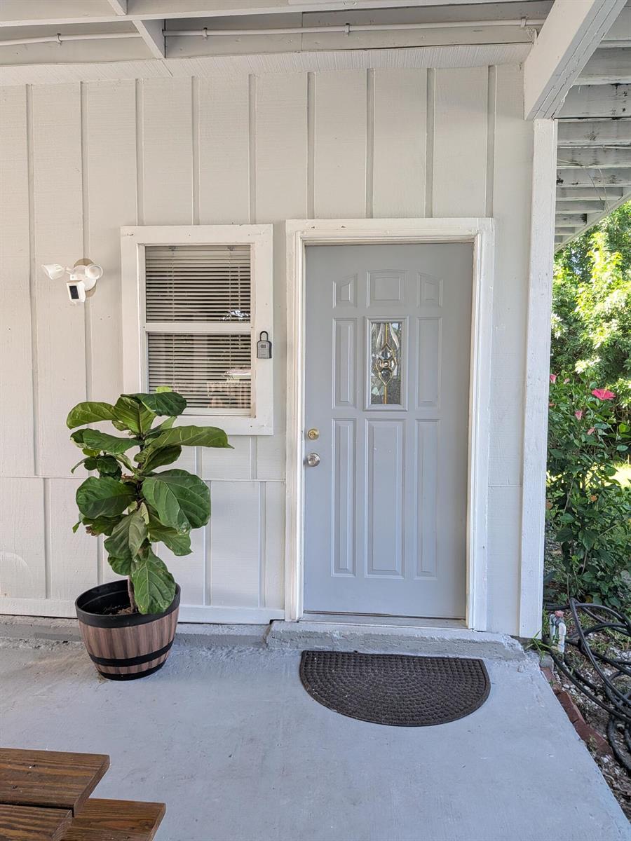 A gray front door with a decorative window sits beside a window and potted plant — 1866 9th Place, Vero Beach FL 32960, VERO BEACH, FL