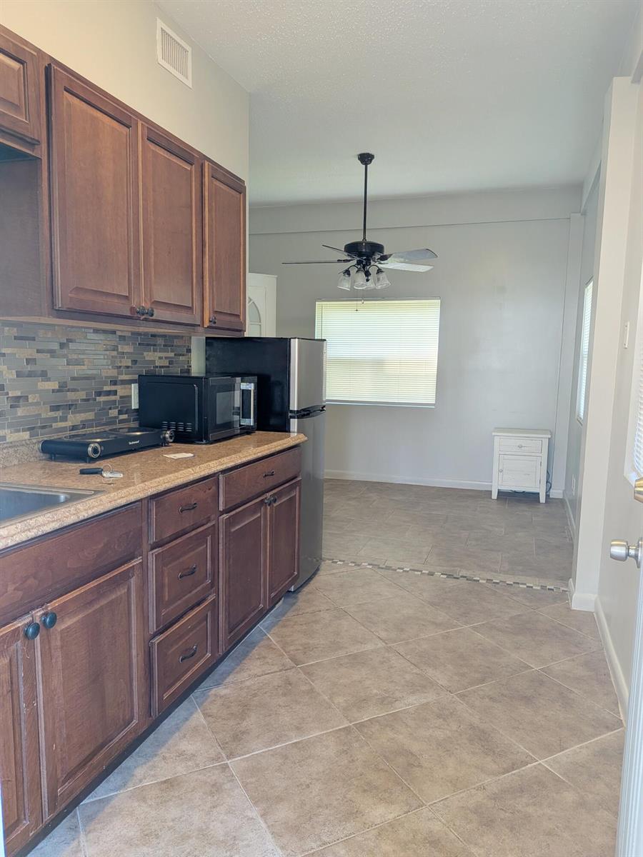 A kitchen features dark wood cabinets, a tiled backsplash, and an adjacent dining area — 1866 9th Place, Vero Beach FL 32960, VERO BEACH, FL