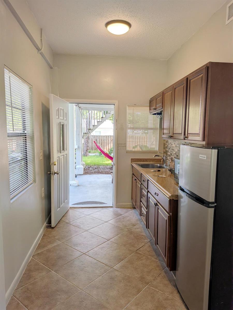 A galley kitchen with wood cabinets, granite countertops, and an open door to a patio — 1866 9th Place, Vero Beach FL 32960, VERO BEACH, FL