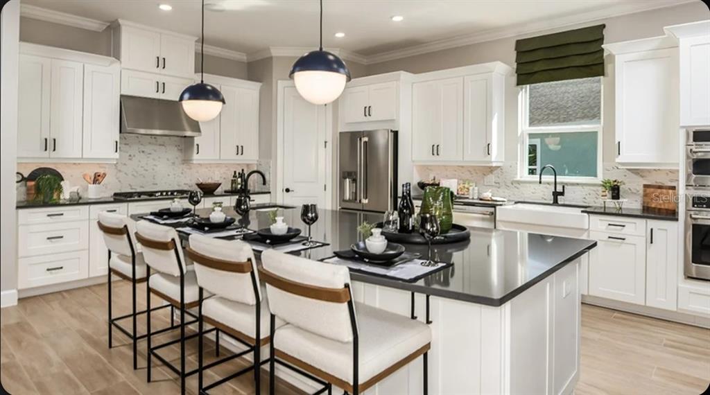 A modern kitchen features white cabinetry, a large dark-topped island, and four upholstered bar stools — 1039 TASSLEFLOWER TRAIL, ST CLOUD, FL
