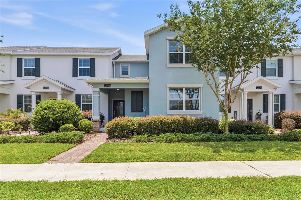 A two-story townhouse exterior with light blue siding, white trim, and a landscaped front yard — 12140 SONNET AVENUE, ORLANDO, FL