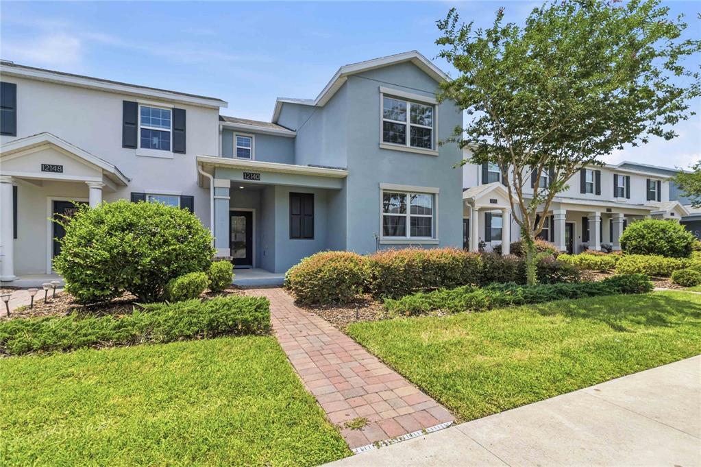 A two-story townhouse with a light blue exterior, a brick walkway, and manicured landscaping — 12140 SONNET AVENUE, ORLANDO, FL