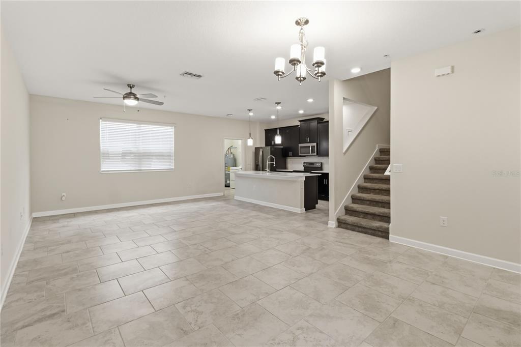 An open-concept living room and kitchen featuring tile flooring, dark cabinetry, and a staircase — 12140 SONNET AVENUE, ORLANDO, FL