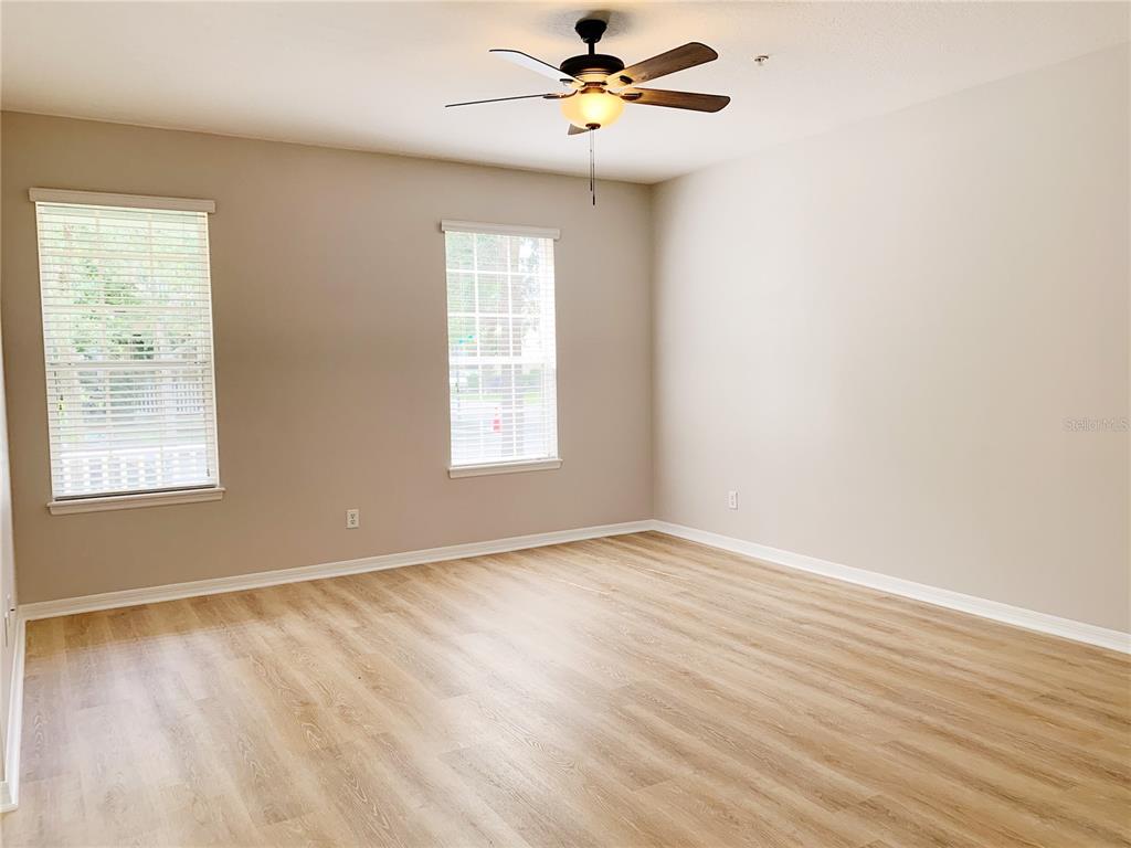 An empty room features light wood-look flooring, beige walls, two windows, and a ceiling fan — 10353 LAKE DISTRICT LANE UNIT 56C, ORLANDO, FL