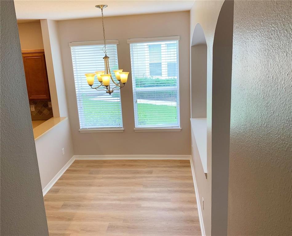 A dining area features light wood-look flooring, a chandelier, and two windows with blinds — 10353 LAKE DISTRICT LANE UNIT 56C, ORLANDO, FL